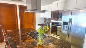 A modern kitchen with a marble island, stainless steel appliances, and a vase of flowers.