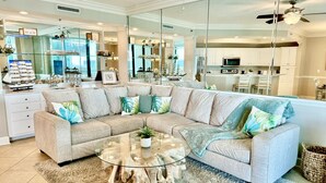 A modern living room with a sectional sofa, a glass coffee table, and a kitchen in the background. - Float The Stress Away & Enjoy The Lazy River. Pet Friendly Condo On 5th Floor (Orange Beach)