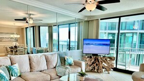 A modern living room with a sectional sofa, a glass coffee table, and a flat-screen TV. - Float The Stress Away & Enjoy The Lazy River. Pet Friendly Condo On 5th Floor (Orange Beach)