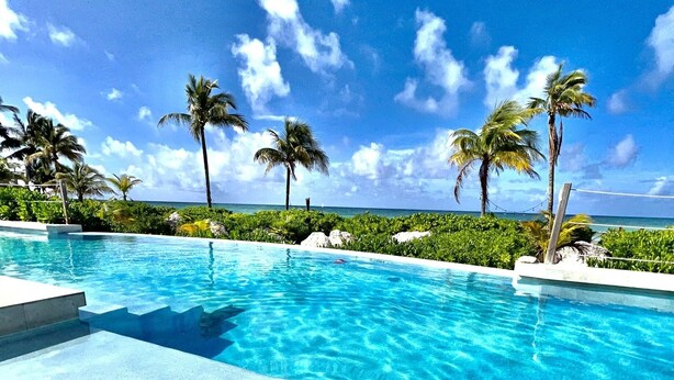 A poolside view with a clear sky, palm trees, and a calm pool. - GoldenEye Estates!- GoldenEye + Palm Villas (Freeport)