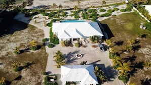 An aerial view of a coastal property with a large white building, a swimming pool, and a beach. - GoldenEye Estates!- GoldenEye + Palm Villas (Freeport)