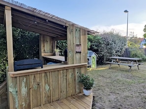 A wooden deck with a built-in barbecue area, a small seating area, and a picnic table in a backyard setting. - Family Villa for 8 people (Seignosse)