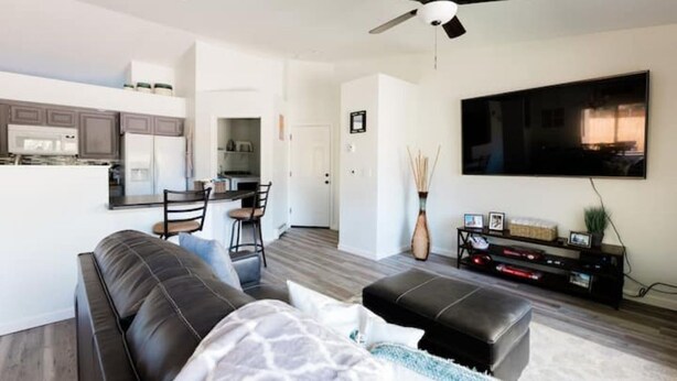 Una sala de estar moderna con un sofá de cuero negro, una mesa de centro y un televisor de pantalla plana montado en la pared.