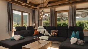 A modern living room with a sectional sofa, a wooden coffee table, and large windows offering a view of greenery.