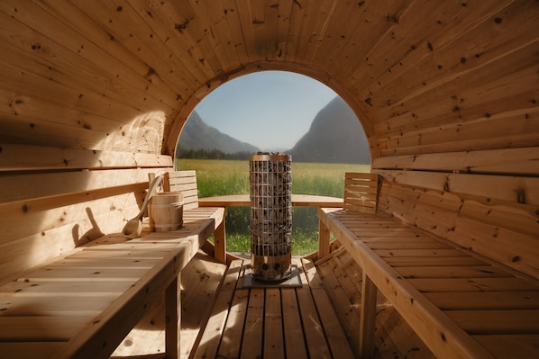 A wooden cabin with a circular opening, wooden benches, a central table, and a view of mountains.