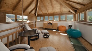 A wooden interior with a high ceiling, a dining table, seating, and a view through large windows.