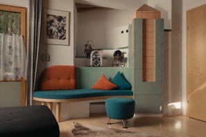 A room with a teal sofa, a small ottoman, a wooden door, and a window with a curtain.