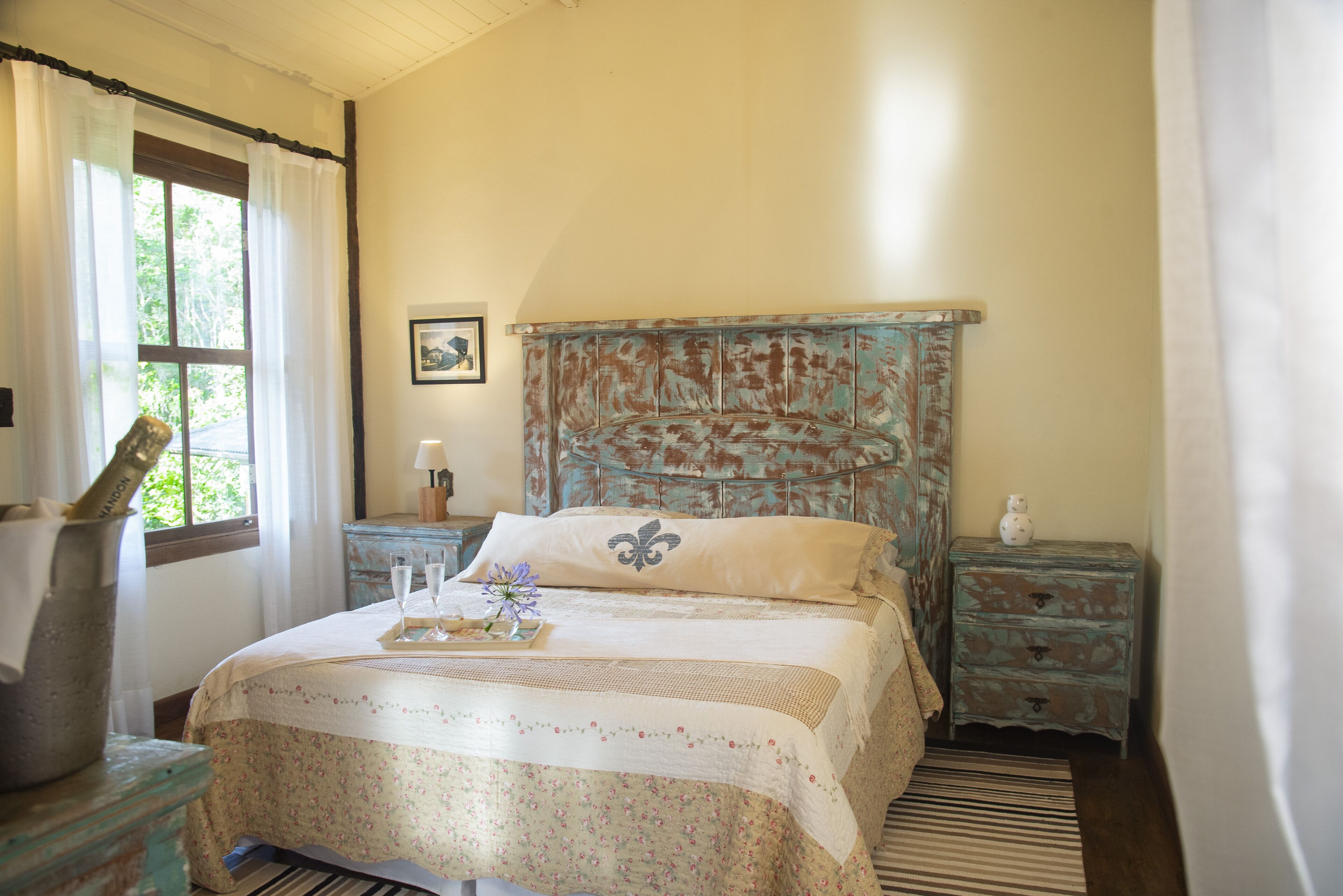 A bedroom with a bed, a nightstand, a dresser, a window with curtains, and a framed picture on the wall.