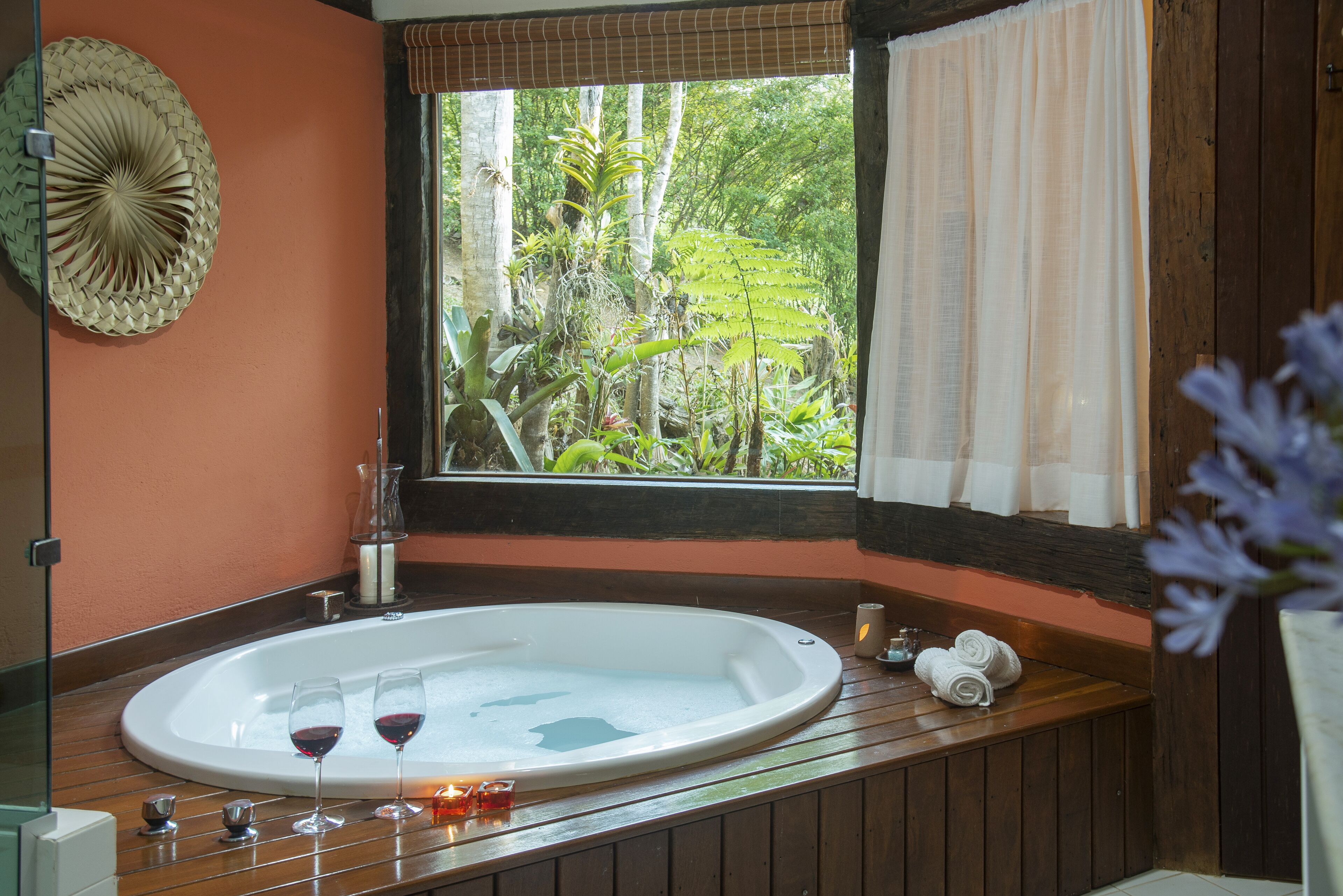 A bathroom with a large bathtub, a window with a view of greenery, and a wooden vanity.
