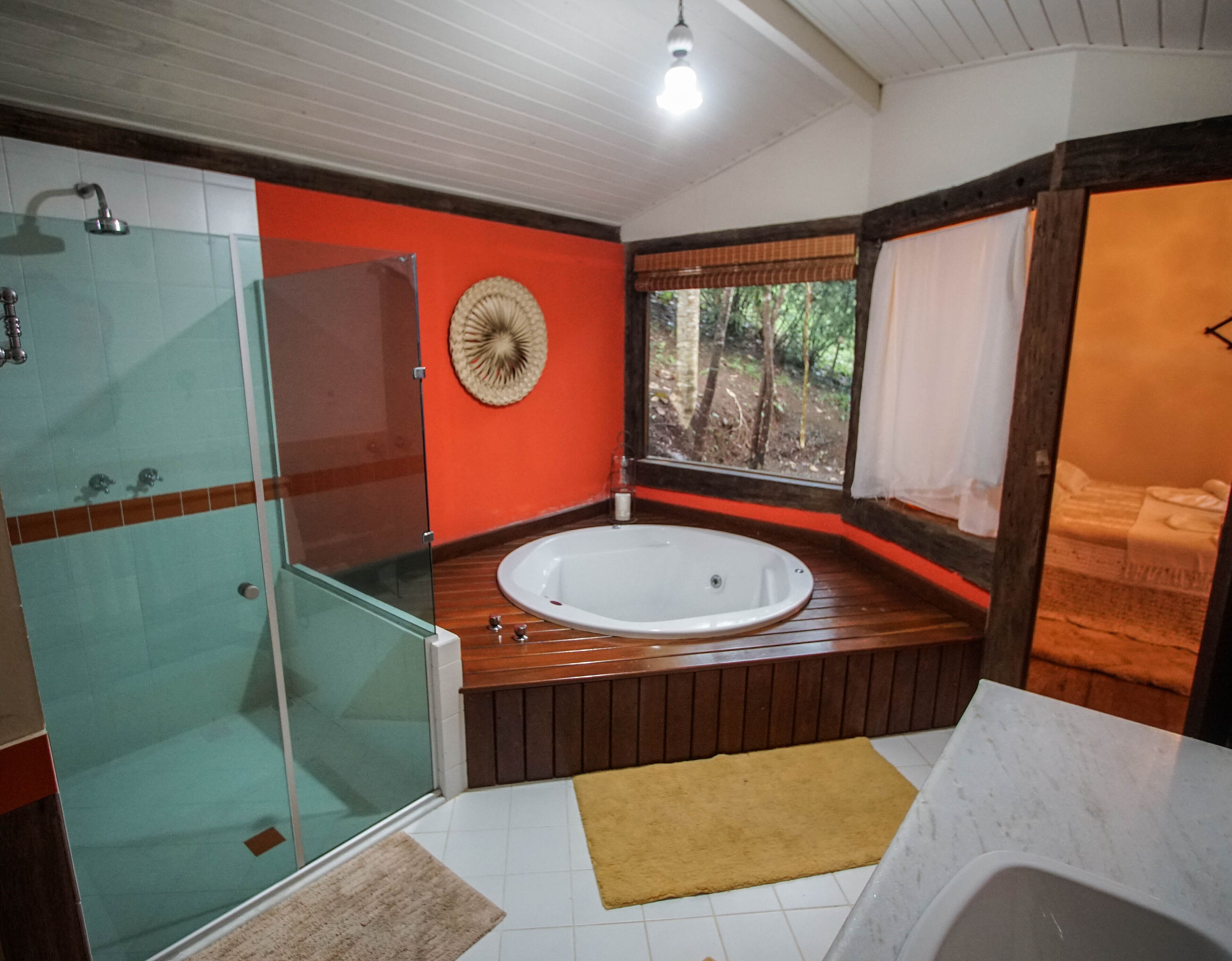 A bathroom with a glass shower enclosure, a wooden bathtub, and a window with a view of trees.