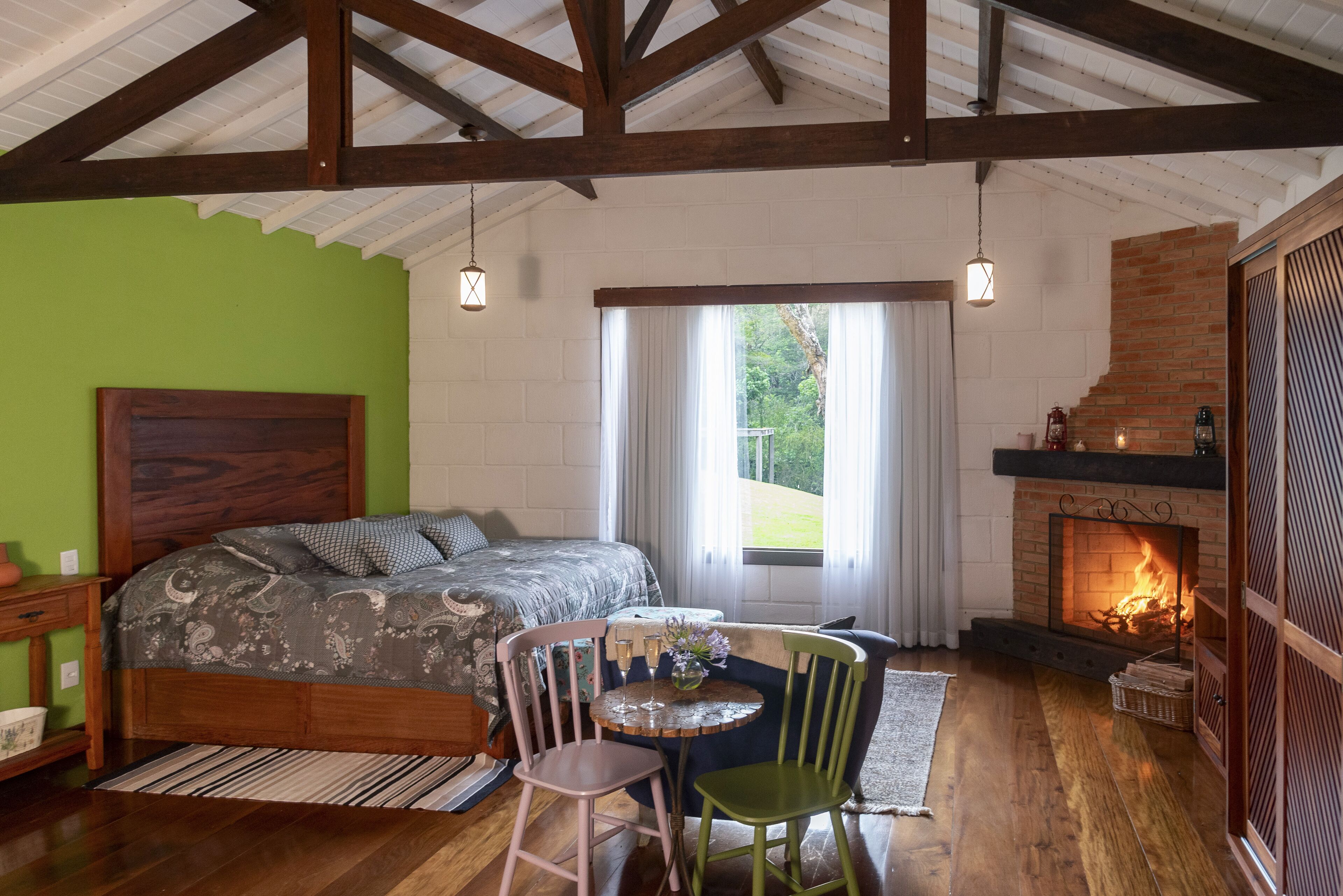 Un dormitorio con cama, chimenea, mesa de comedor con sillas y ventana con cortinas.