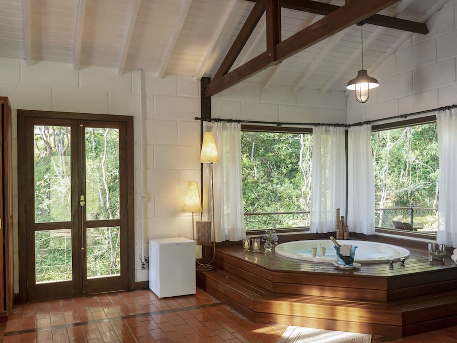 Ein Badezimmer mit einer Badewanne, einem kleinen Kühlschrank und einem Fenster mit Vorhängen.