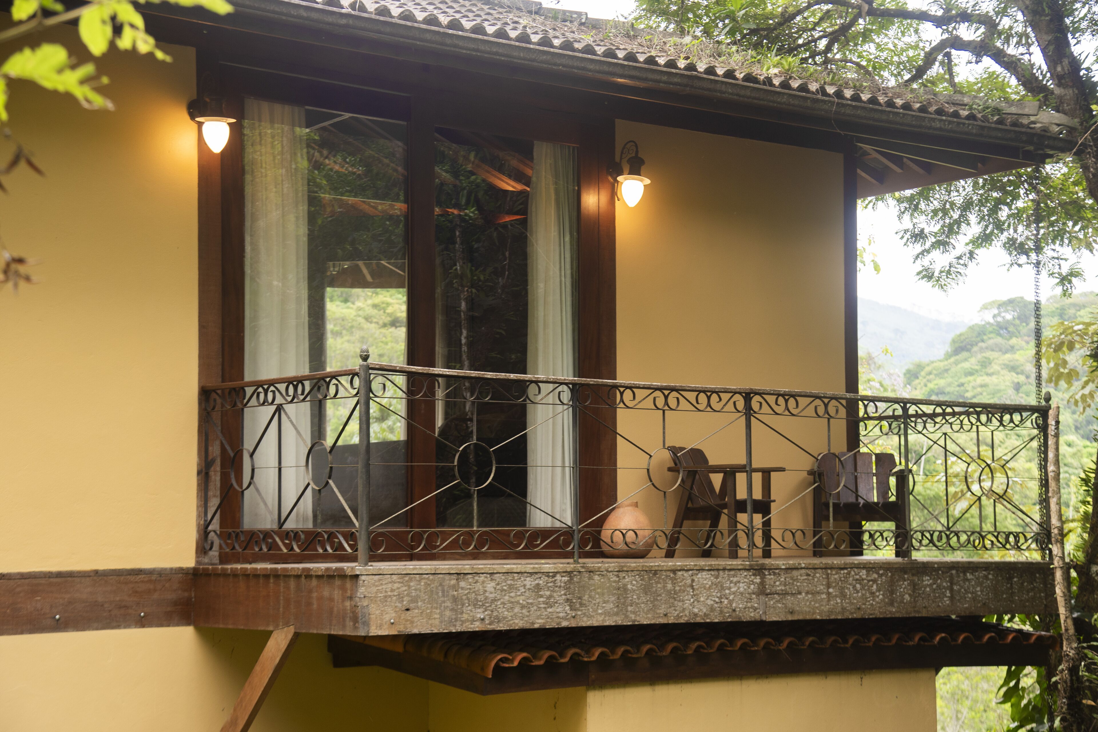 A balcony with a wrought iron railing, a wooden chair, and a table.