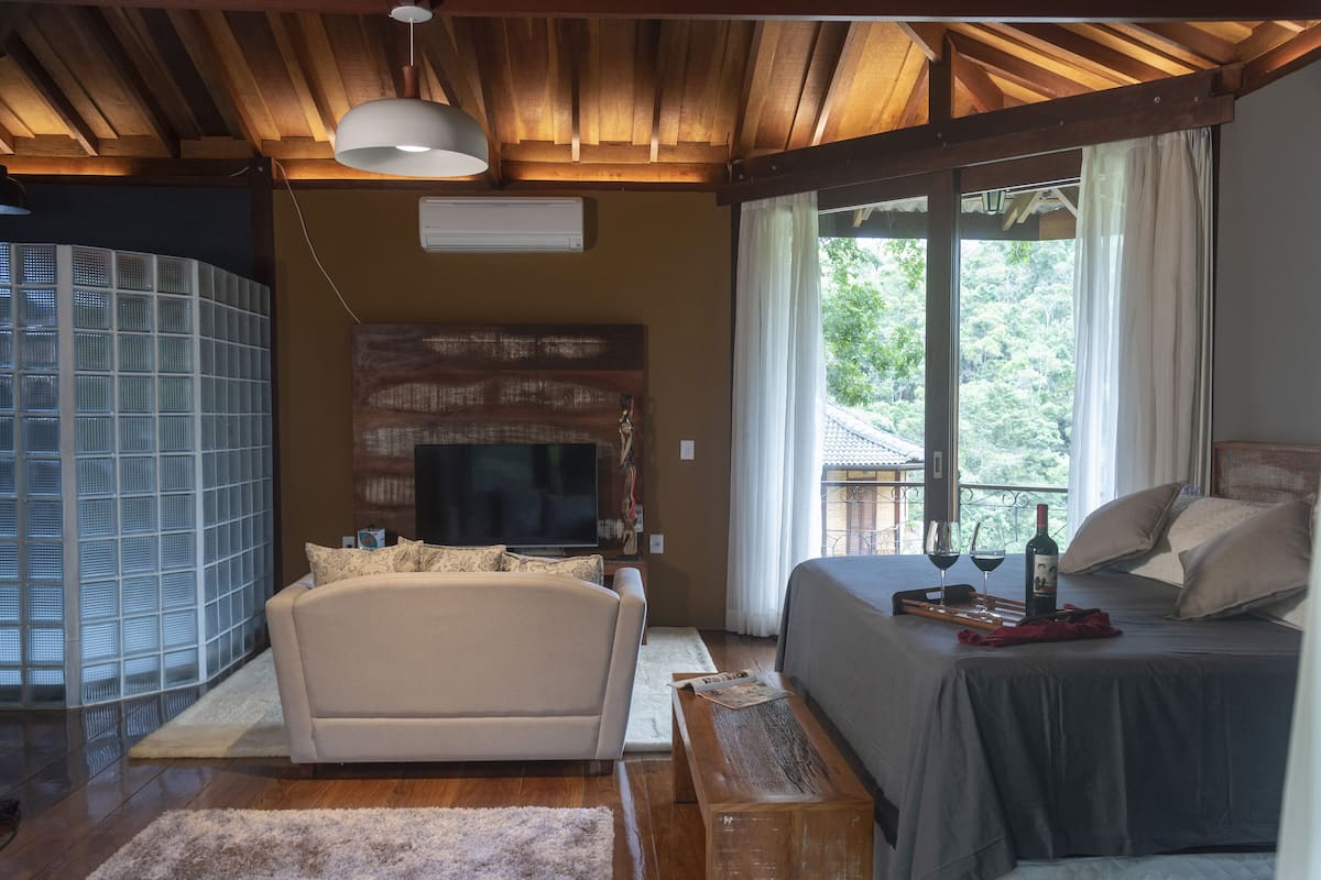 Quarto com cama, sofá, televisão e janela com cortinas.