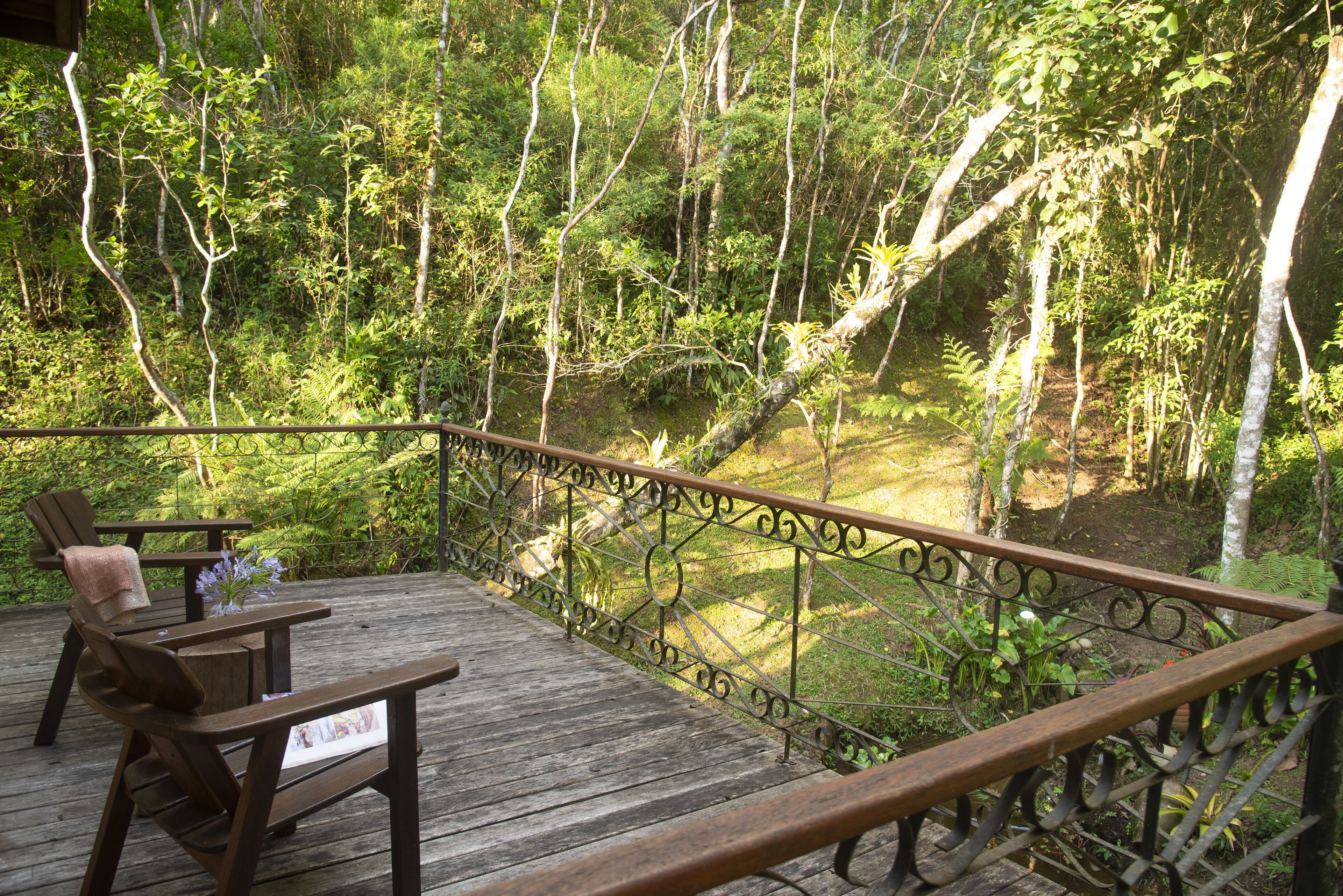 A wooden deck with a metal railing, two wooden chairs, and a table with a vase of flowers.