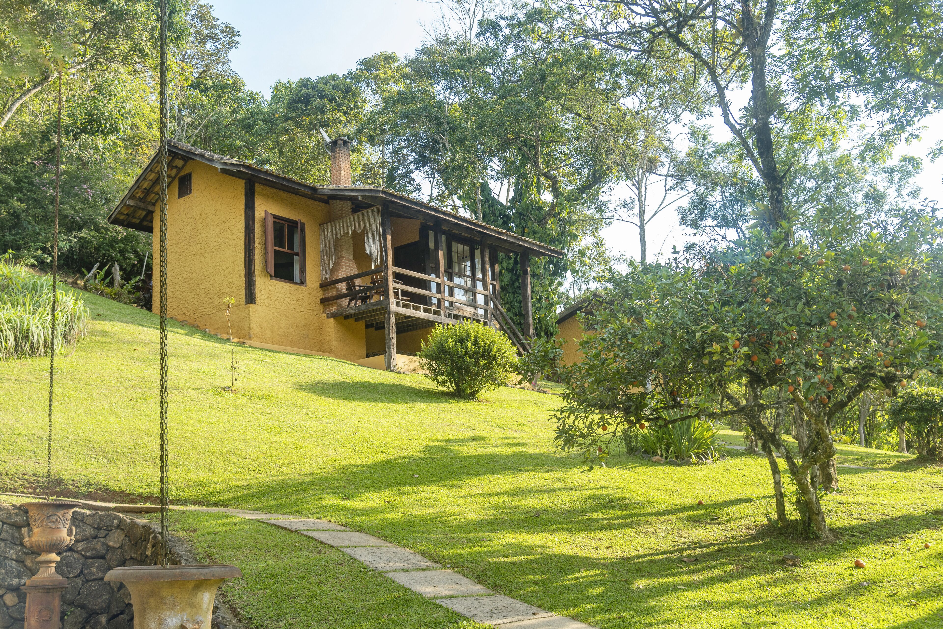 A two-story house with a balcony, surrounded by greenery and a stone pathway.