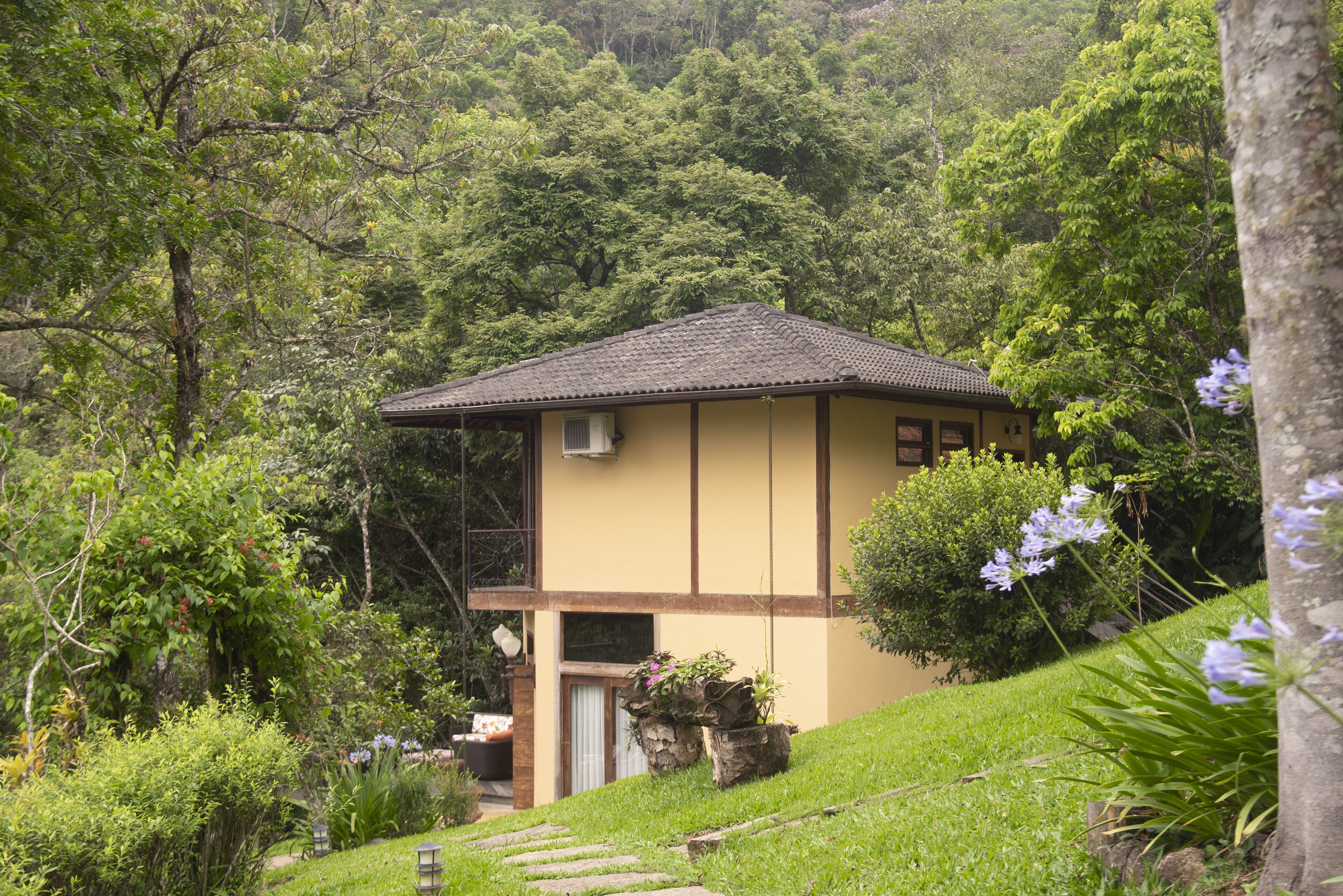 A two-story building with a tiled roof, surrounded by lush greenery and trees.