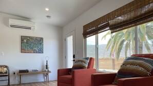 Una sala de estar con dos sillones rojos, una mesa de centro de madera y un ventanal con vistas a palmeras.
