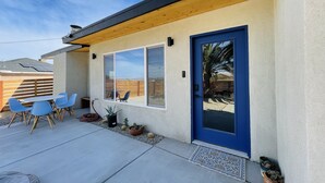 Una casa moderna con puerta azul, un patio con sillas azules y vista al jardín trasero.