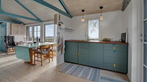 Une cuisine avec une table et des chaises en bois, une fenêtre donnant sur un beau paysage et un meuble de couleur turquoise doté de tiroirs.