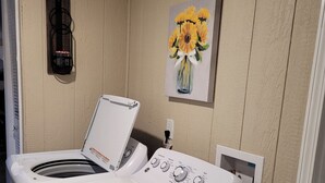 Une buanderie équipée d’un lave-linge et d’un sèche-linge à chargement frontal, d’un luminaire fixé au mur et d’un tableau représentant des fleurs jaunes.