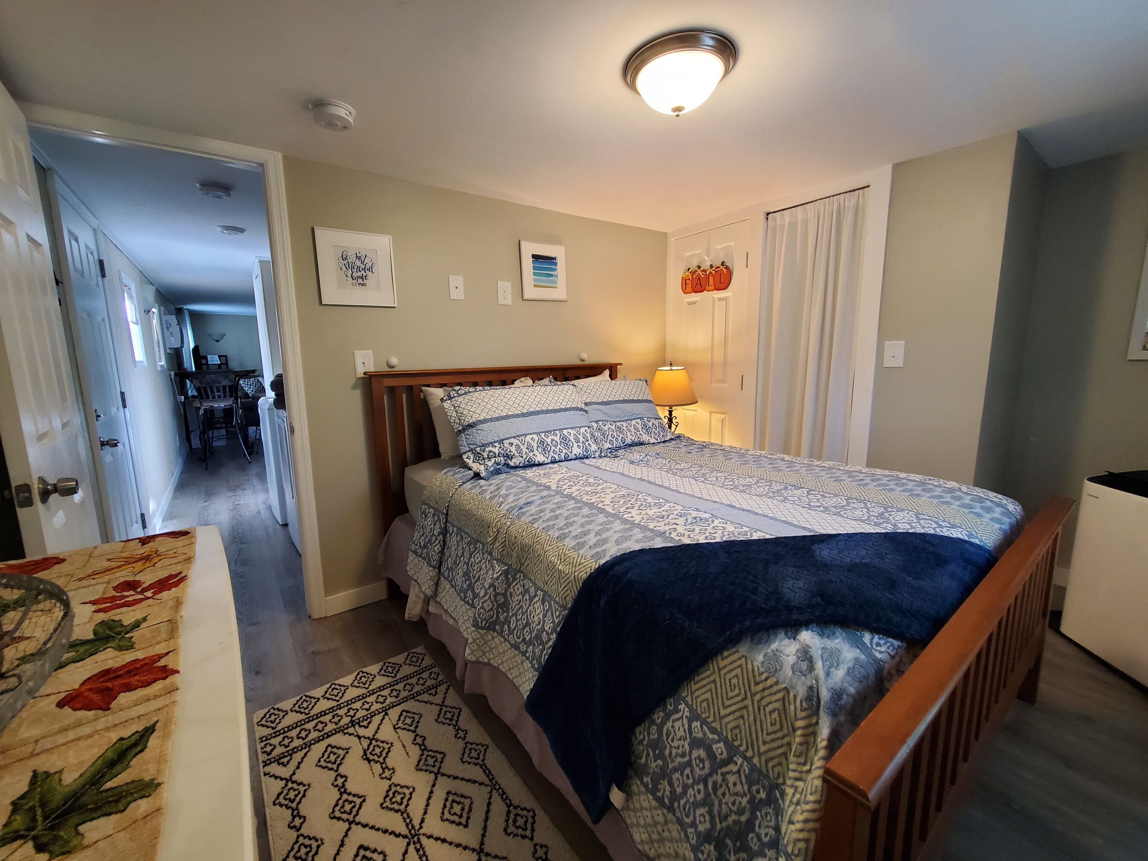 Een slaapkamer met een bed, een bedlampje, een vloerkleed en een deur naar een gang.