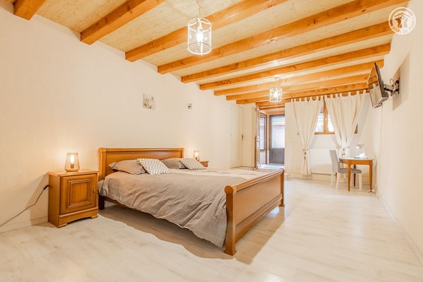 A bedroom with a wooden bed, bedside lamps, a desk with a chair, and a window with curtains.