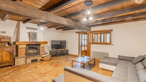 A rustic living room with exposed wooden beams, a fireplace, a sofa, and a television. - Domaine du Venet - Montcony (MONTCONY)