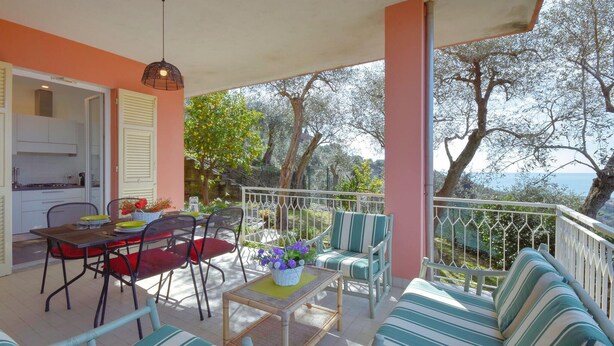 A covered outdoor seating area with a table and chairs, a sofa, and a view of trees and the sea. - Gorgeous apartment in San Bartolomeo di Leiv (San Bartolomeo di Leiv)