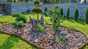 A landscaped garden with a variety of plants, a wooden sculpture, and a stone wall in the background.