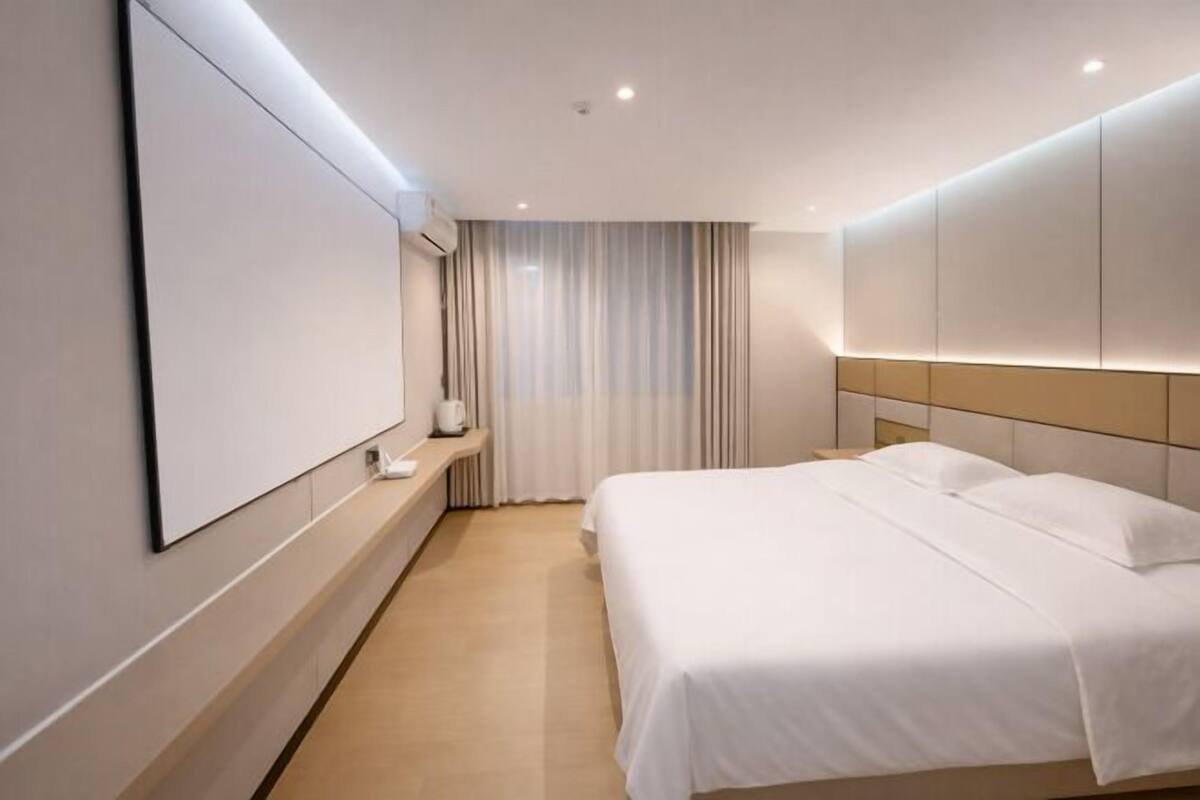 Een hotelkamer met een bed, een flatscreen-tv, een nachtkastje en een raam met gordijnen.