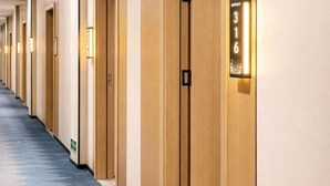 Een hotelgangen met houten deuren, genummerde kamerindicaties en een vloerkleed.