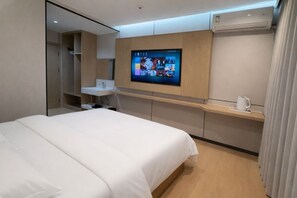 Une chambre d’hôtel moderne avec un grand lit, un téléviseur fixé au mur, une petite table de chevet et une étagère intégrée.