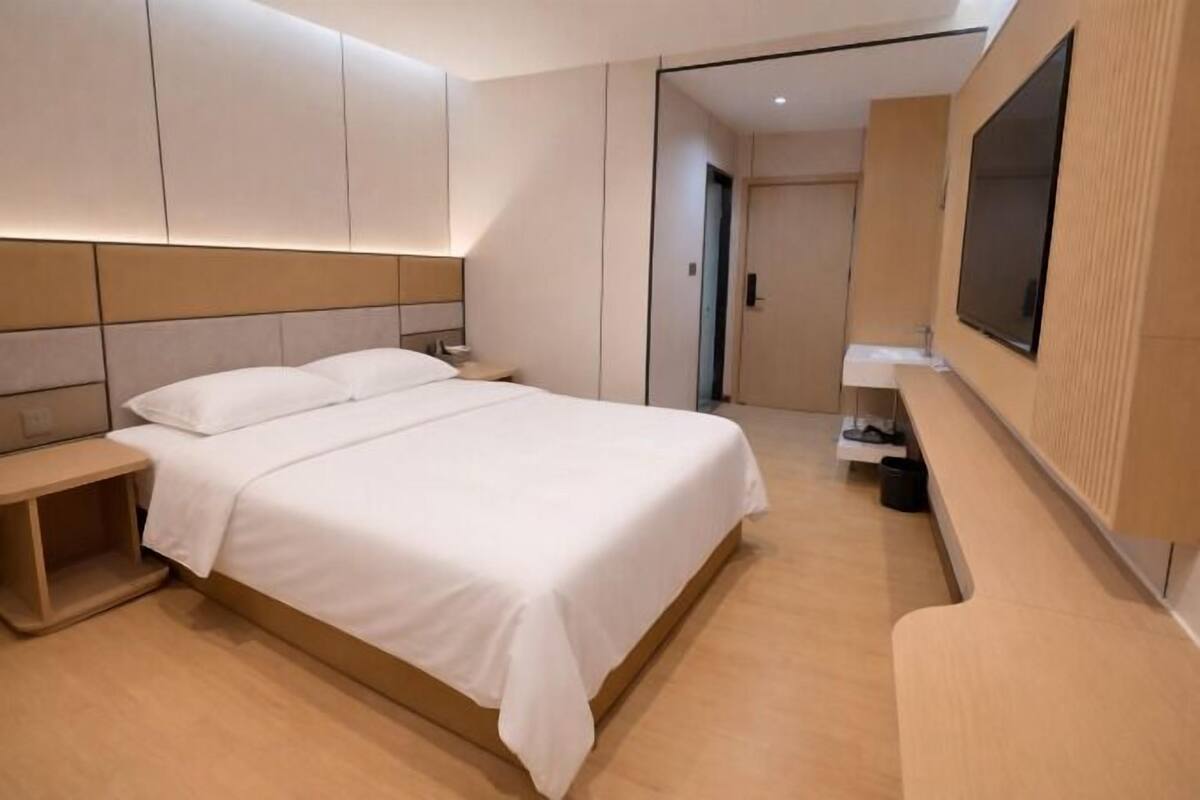 Een moderne hotelkamer met een groot bed, nachtkastjes, een aan de muur bevestigde televisie en een kleine badkamerruimte.
