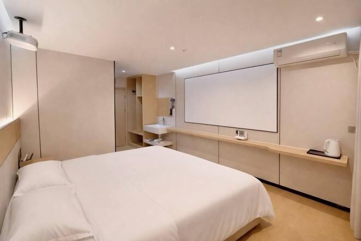 Een moderne hotelkamer met een bed, een ingebouwde televisie, een nachtkastje en een kledingkast.
