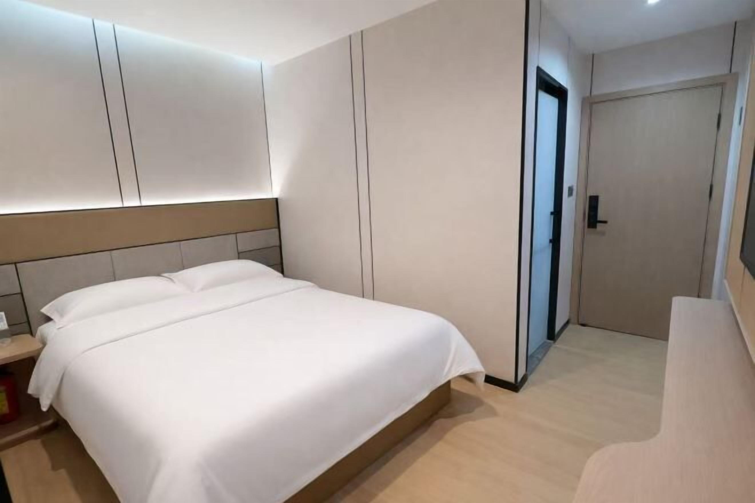 A modern hotel room with a large bed, built-in wardrobe, and a door leading to a bathroom.