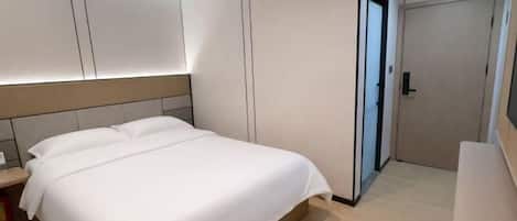 A modern hotel room with a large bed, built-in wardrobe, and a door leading to a bathroom.