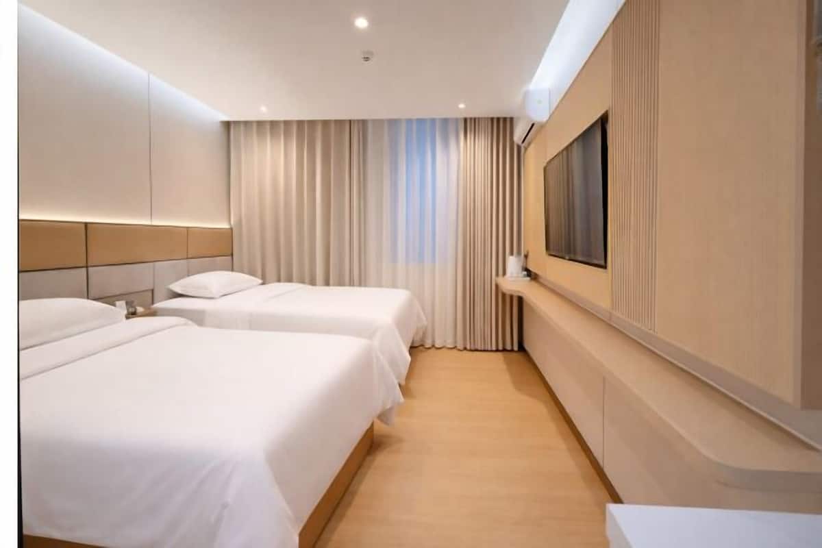 Een hotelkamer met twee bedden, een televisie en een groot raam met gordijnen.