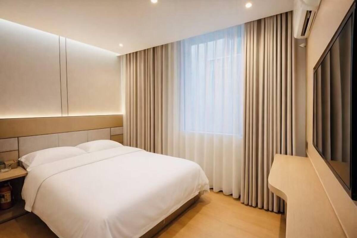 Hotelkamer met een groot bed, nachtkastje, raam met gordijnen en een wandgemonteerde airconditioning.