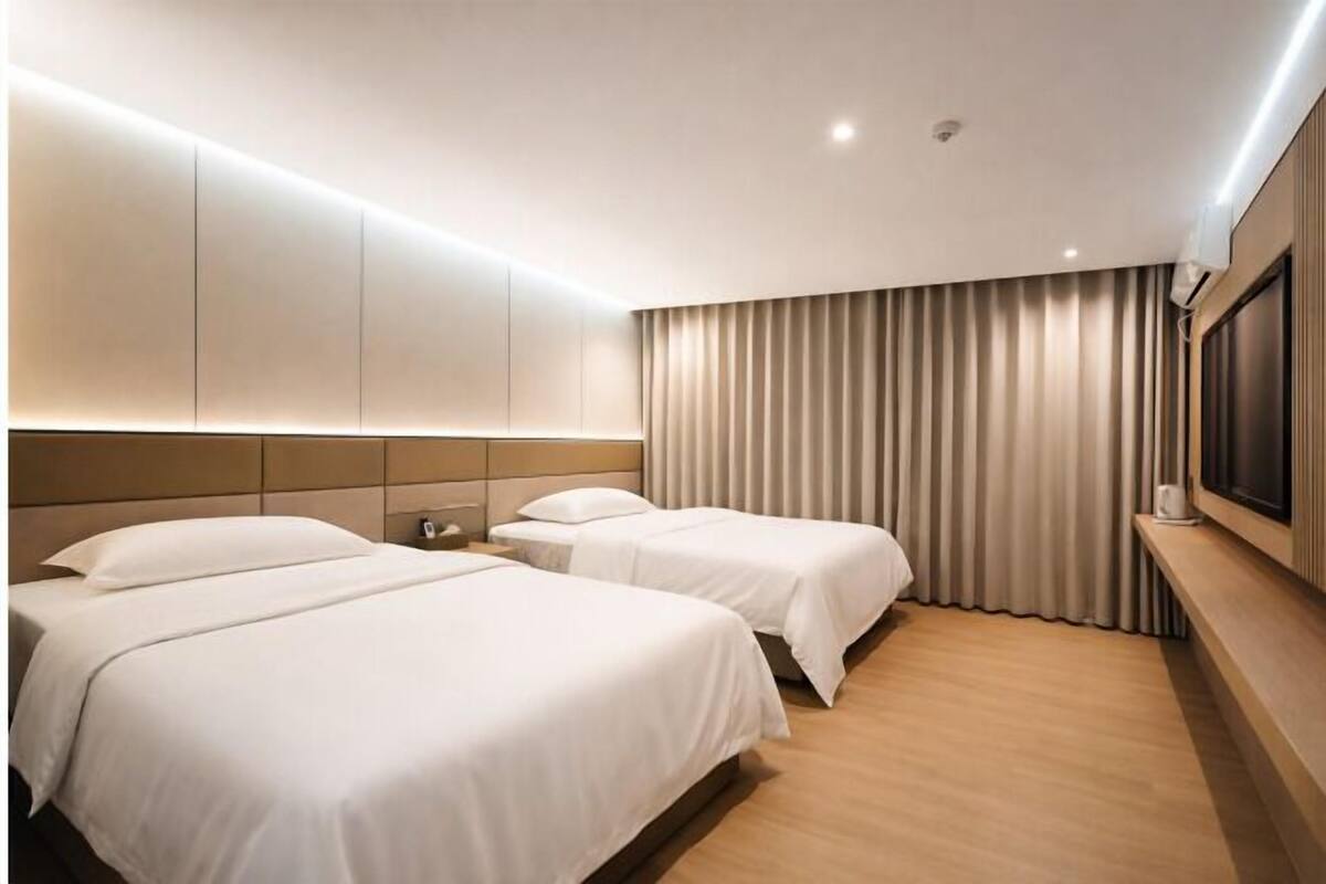 Een hotelkamer met twee bedden, een grote spiegel, een flatscreen-tv en een raam met gordijnen.