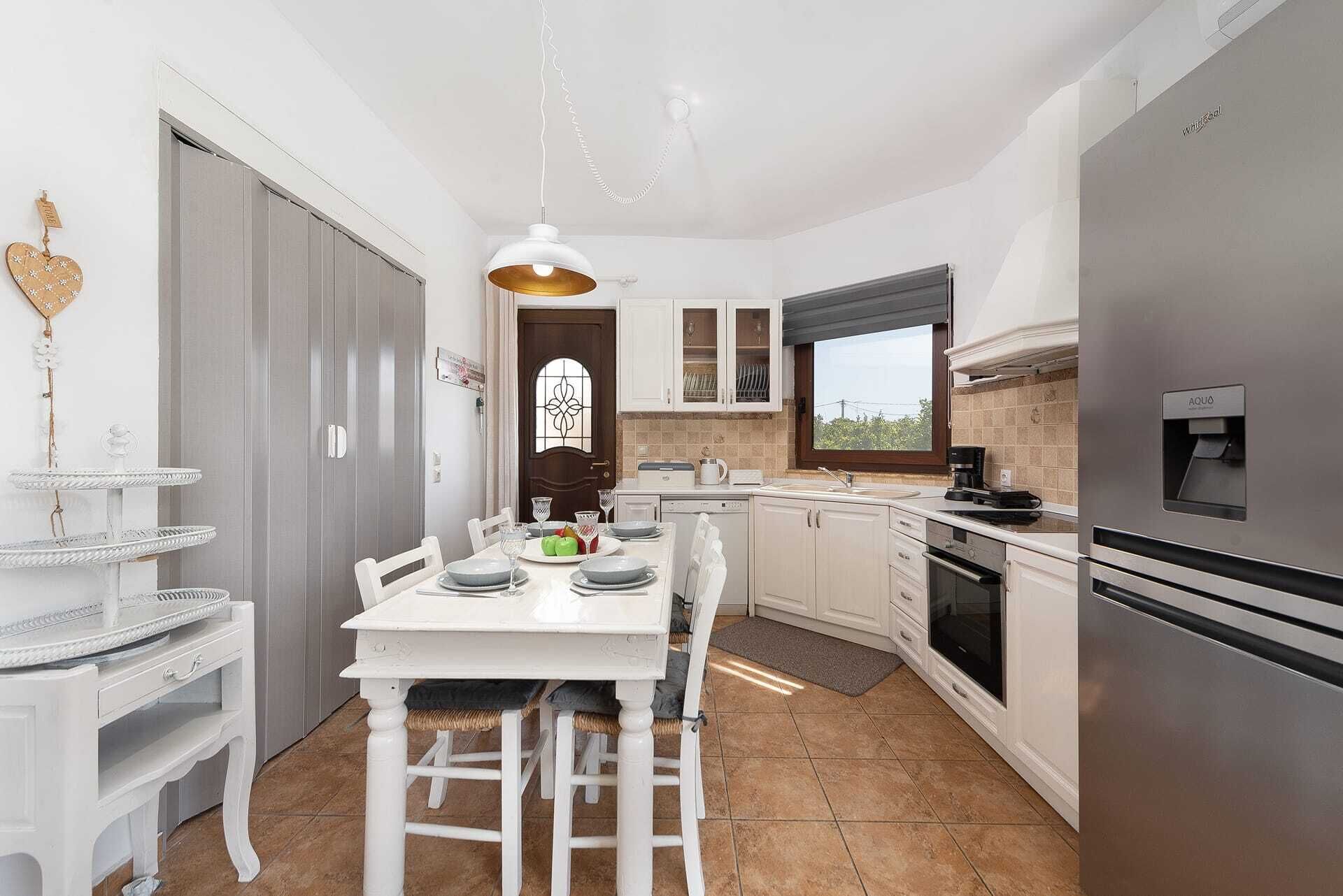 A modern kitchen with white cabinetry, a stainless steel refrigerator, and a dining area with a white table and chairs.