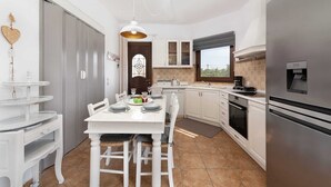 A modern kitchen with white cabinetry, a stainless steel refrigerator, and a dining area with a white table and chairs.