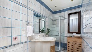 A bathroom with a glass shower enclosure, a sink with a swan-shaped soap holder, and a wooden vanity.