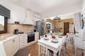 A modern kitchen with white cabinetry, a dining area with a white table set for four, and a stone wall in the background. - Dont miss your chance to experience the magic of Evis Afandou Suite. (Afandou)