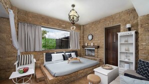 A bedroom with a bed, a small table, a chair, a bookshelf, and a fireplace.