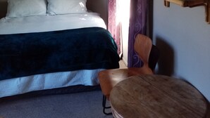 Un dormitorio con cama, una silla, una mesita, un espejo y un cuadro en la pared.
