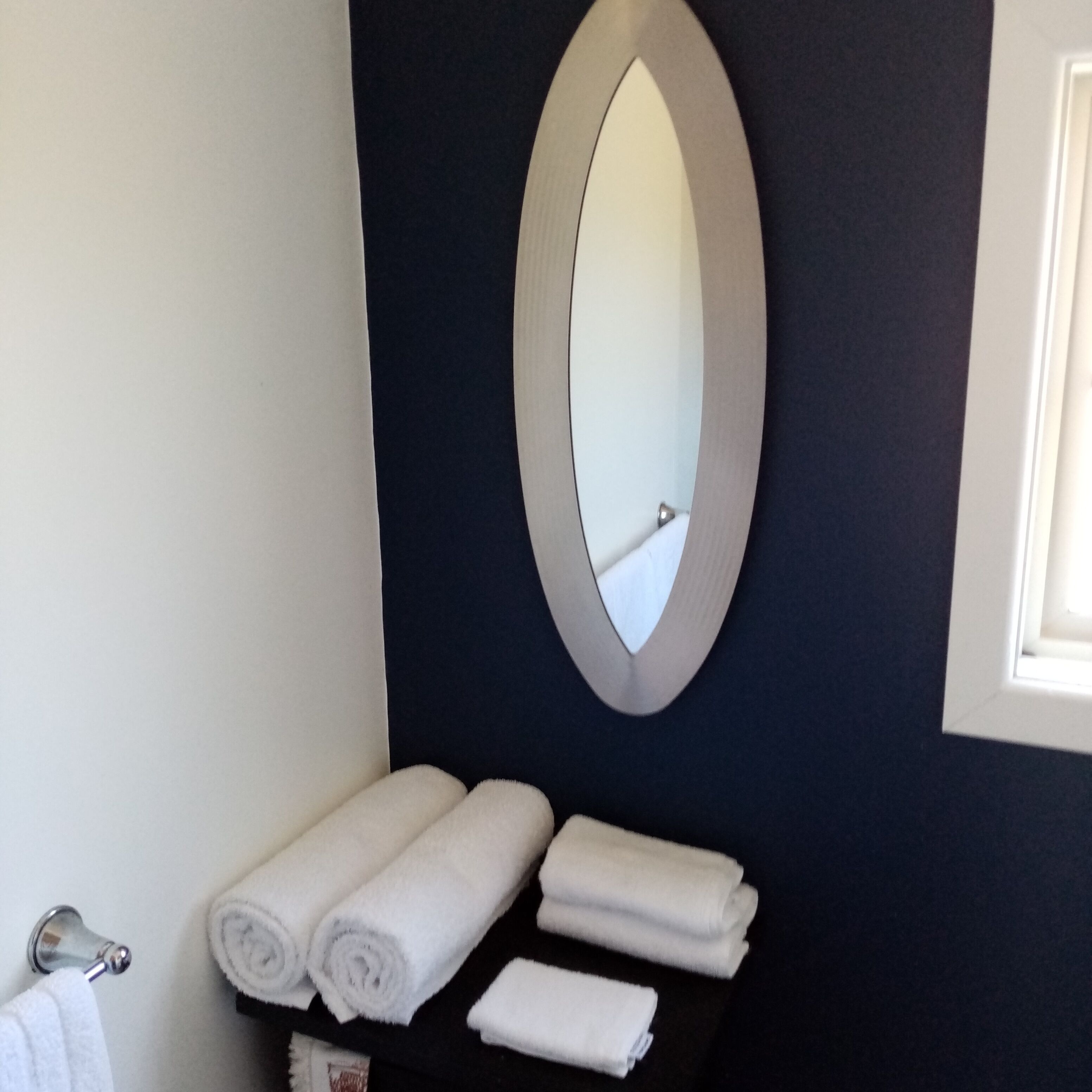 A bathroom with a dark wall, a white sink, and a mirror. There are three rolled towels on the sink.