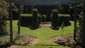 Un jardín con un pérgola, setos bien cuidados y una variedad de plantas.