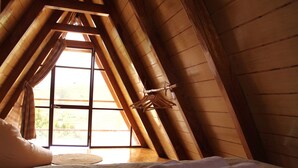 Un dormitorio con techo inclinado, una cama con ropa blanca y un ventanal con cortinas.