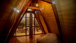 Un dormitorio acogedor en el ático, con techo inclinado, un gran ventanal y un sillón de saco.